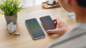 Player comparing two unbranded smartphones on a bright desk with earbuds and a plant.