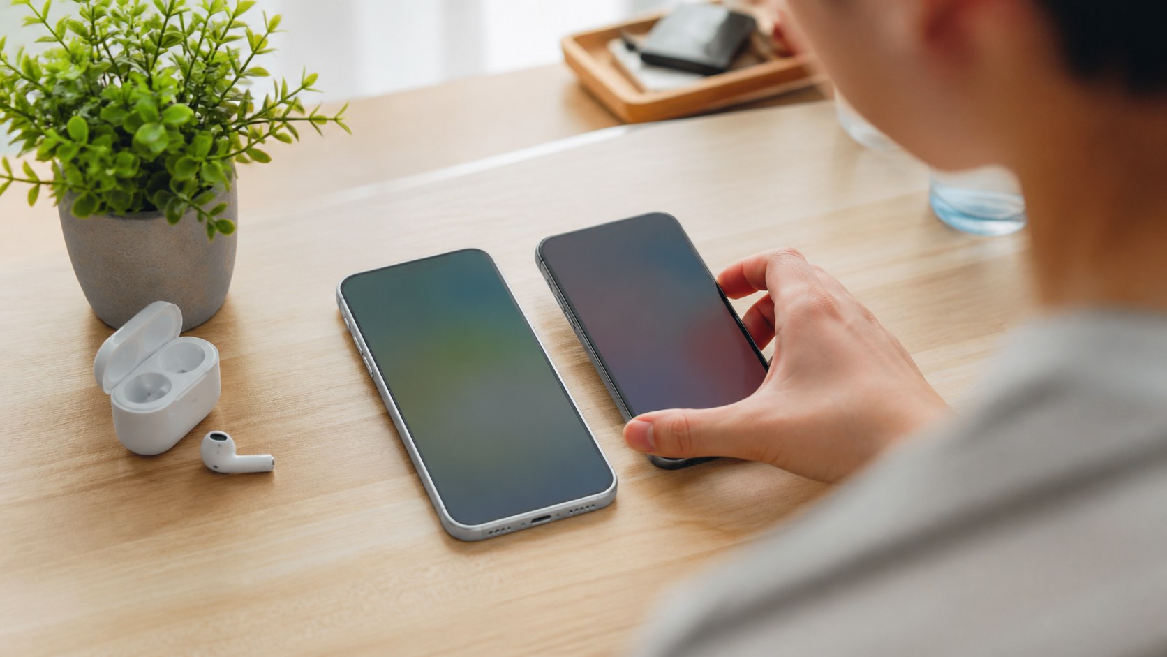Player comparing two unbranded smartphones on a bright desk with earbuds and a plant.