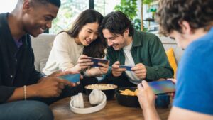 Friends playing mobile games together on unbranded smartphones in a bright lounge.