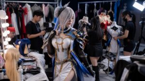 A polished cosplay backstage prep area with costume racks, wigs, makeup, mannequins, and event lighting.